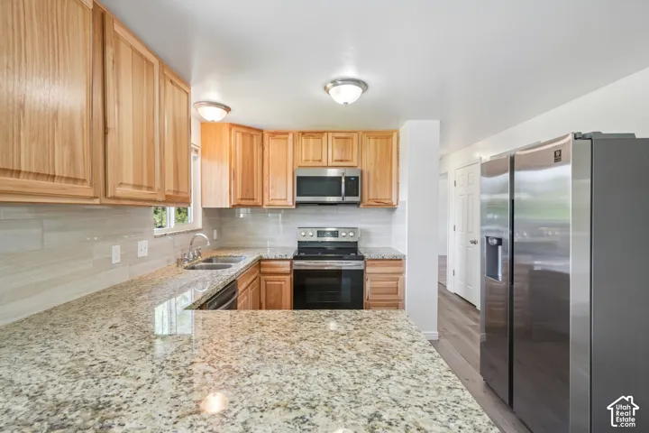 Kitchen featuring granite countertops, wood cabinetry, tile backsplash, stainless steel appliances, and wood-finish flooring