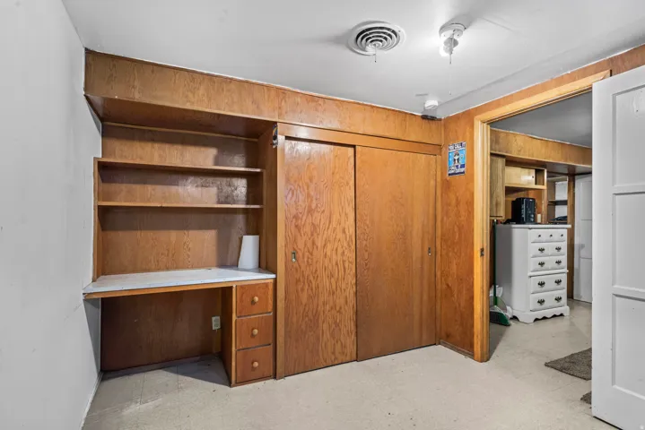 Built-in wood-finish desk with shelving and three drawers, wood-finish paneling, and wood-finish sliding closet doors