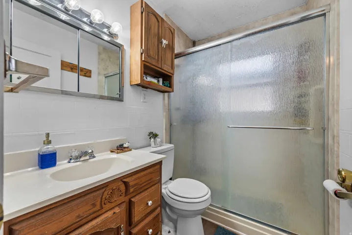 Bathroom featuring a wood-finish vanity with an integrated sink, a mirrored medicine cabinet with vanity lighting, and a shower with a frosted glass enclosure