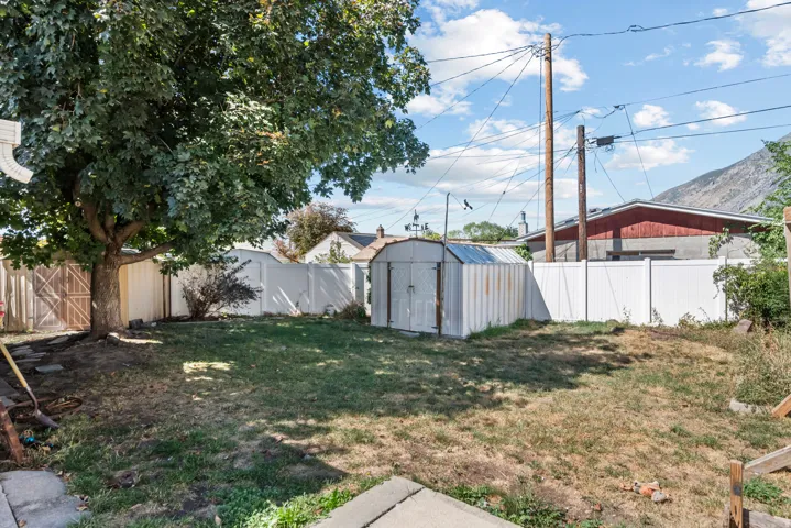 Expansive grassy yard area, mature tree providing natural shade, white privacy fencing, storage shed, and mountain range in the background
