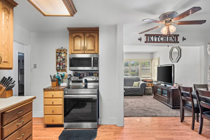 Wood-finish flooring extending into the kitchen, stainless steel range and microwave, and wood cabinetry with brass hardware