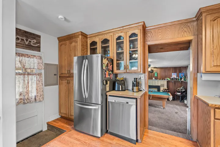 Wood-finish cabinetry with glass-front uppers, stainless steel French door refrigerator, and stainless steel dishwasher