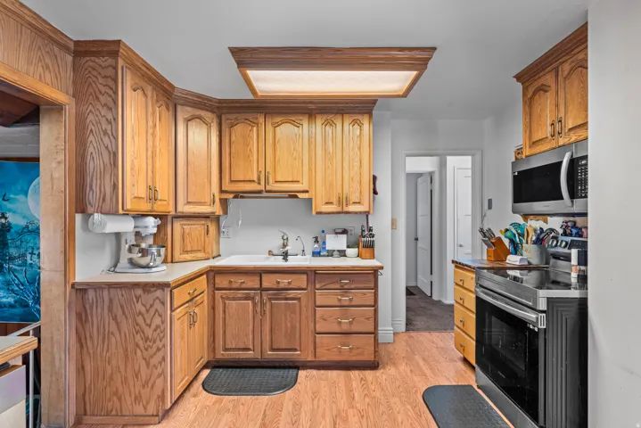 Wood-finish flooring with a U-shaped kitchen layout, featuring wood cabinetry and white countertops, stainless steel microwave, and built-in electric range