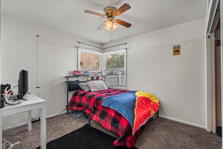 White paneling, carpeted flooring, corner windows with blinds, and a ceiling fan with light fixture