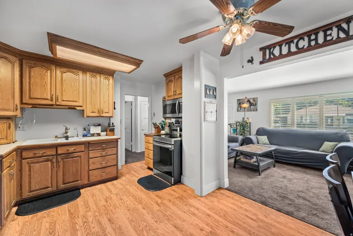 Kitchen featuring wood-finish flooring, wood cabinetry, built-in stainless steel appliances, and a ceiling fan with integrated lighting