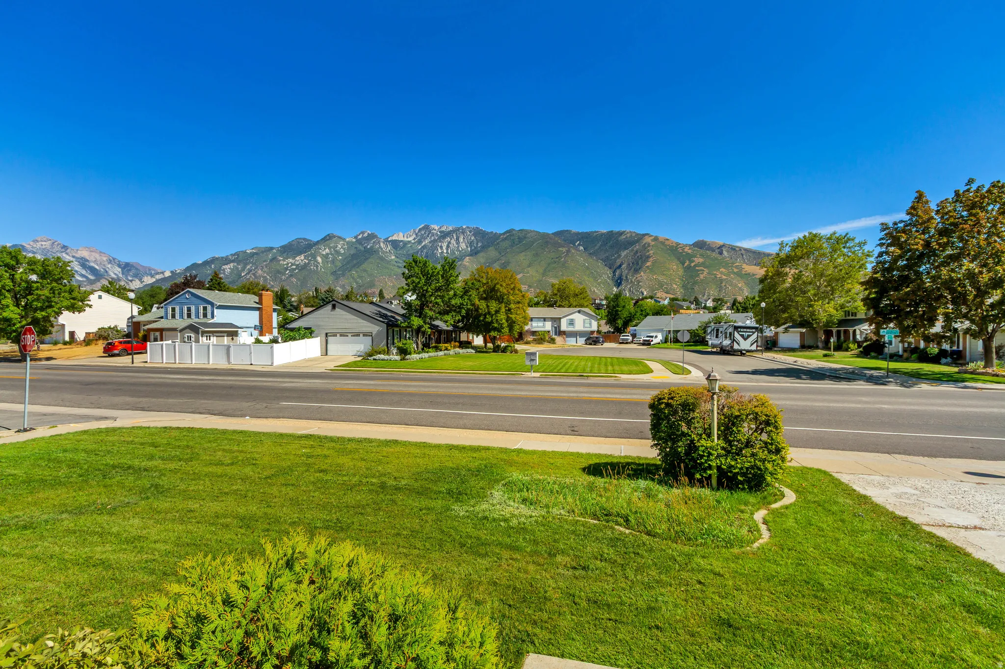 View from the front of Property! Mountain backdrop, street-side location, manicured lawn, established shrubs, clear blue sky