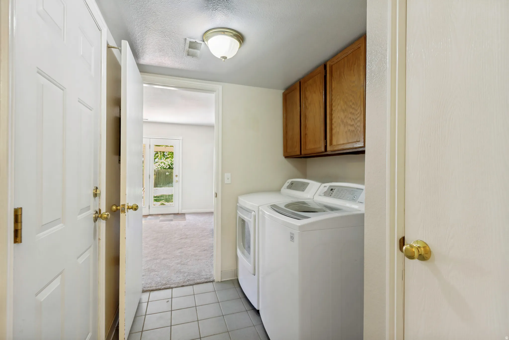Laundry area featuring tile flooring, wood-finish cabinetry, and a ceiling-mounted light fixture
