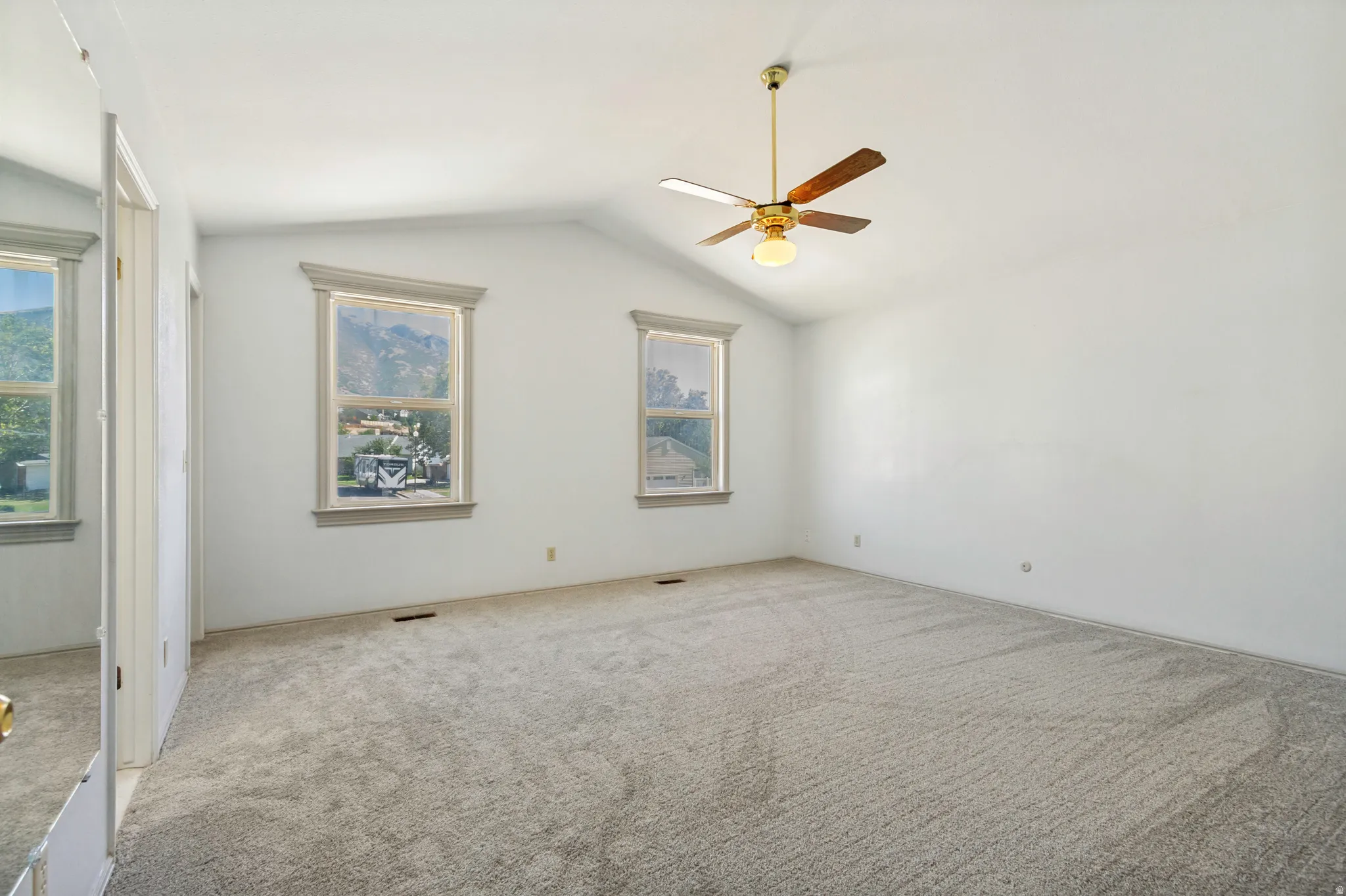 Primary Bedroom - Vaulted ceiling with a ceiling fan light fixture, two windows with decorative trim, and wall-to-wall carpeting