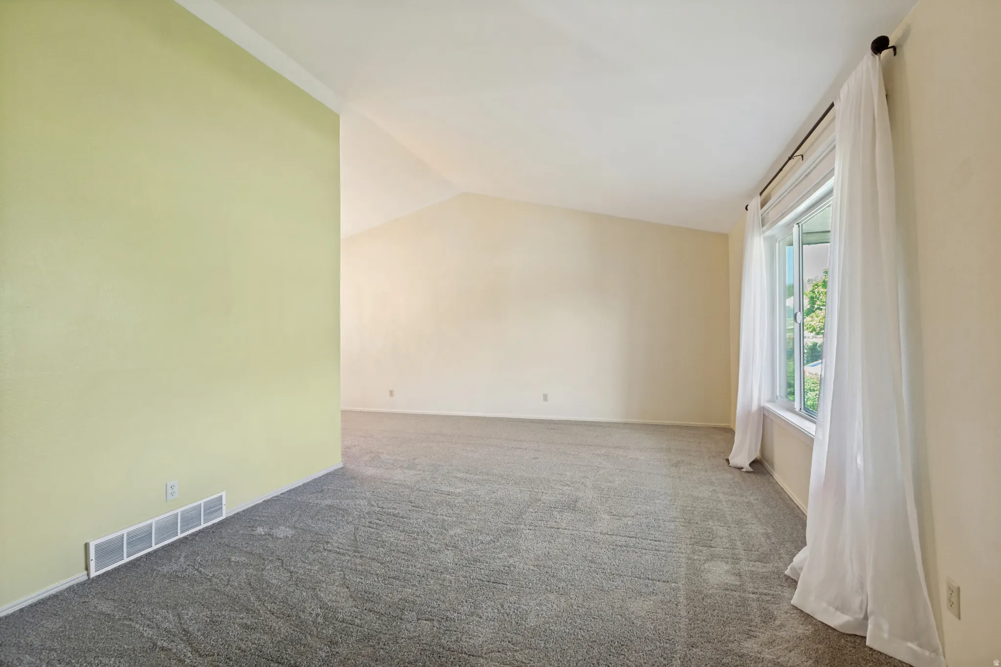 Spacious room with vaulted ceilings, neutral carpeting, and a large window