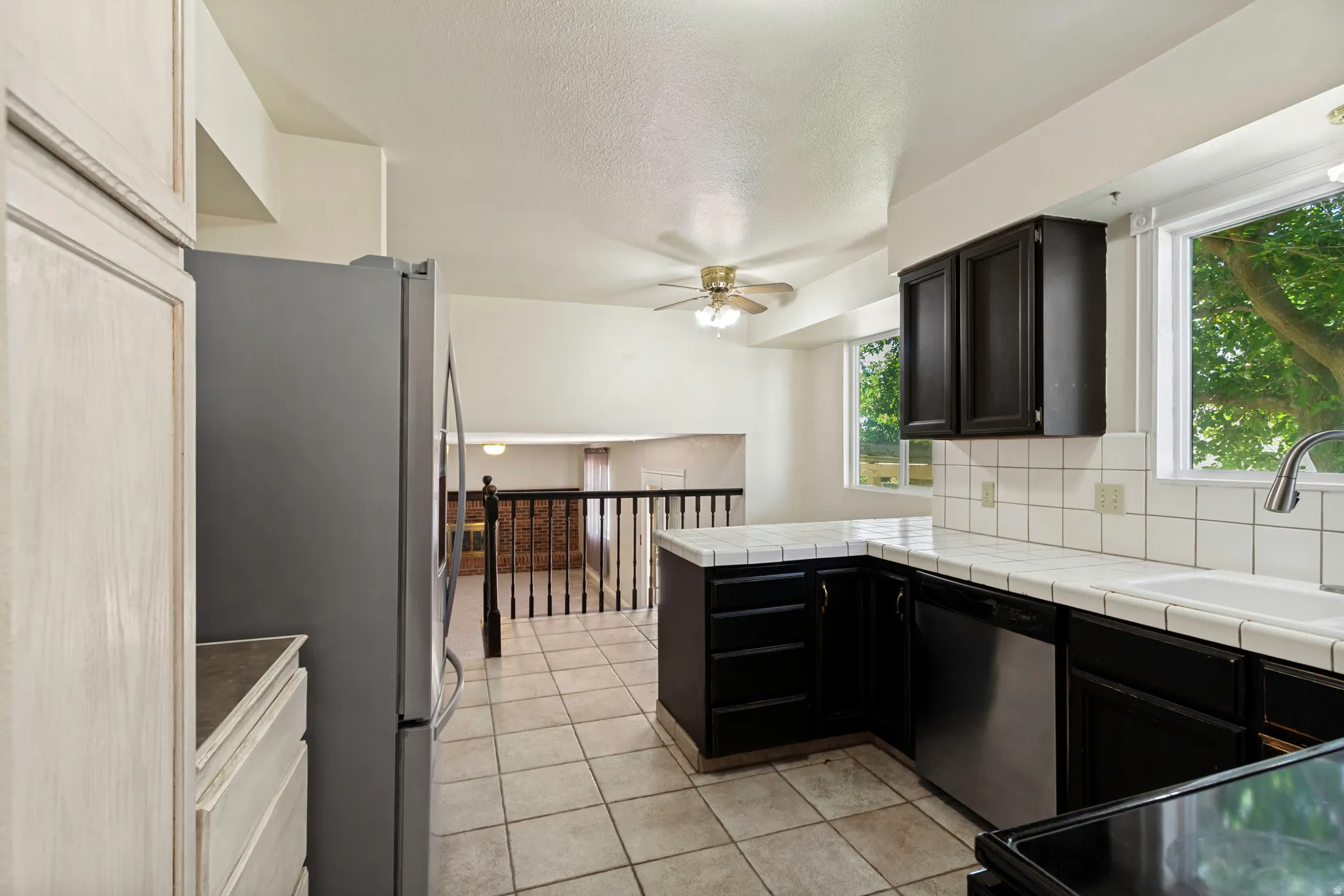 Kitchen featuring tile flooring, white tile countertops, black cabinetry, white tile backsplash, and a ceiling fan