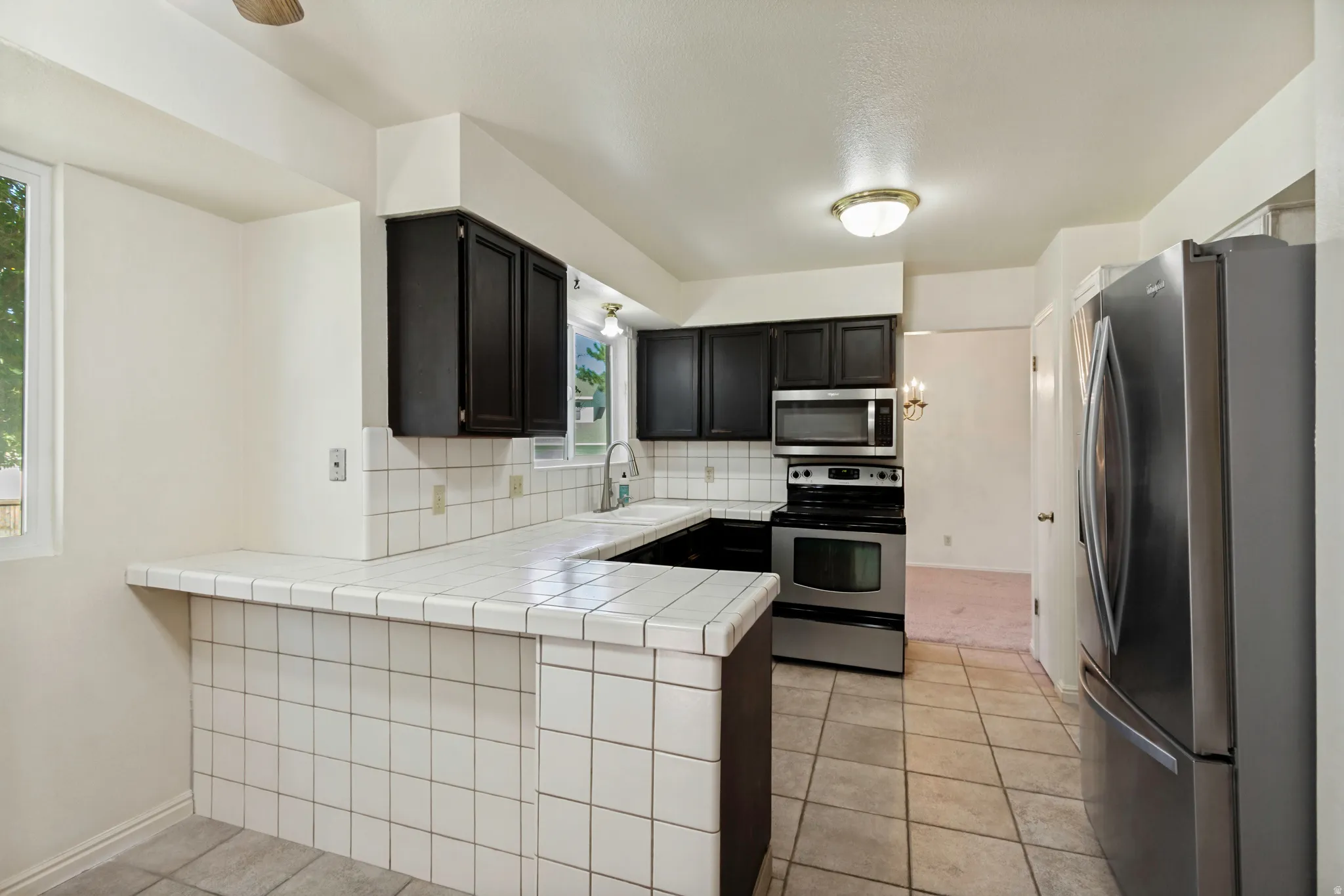 Kitchen featuring white tile countertops, dark cabinetry, stainless steel appliances, and tile flooring