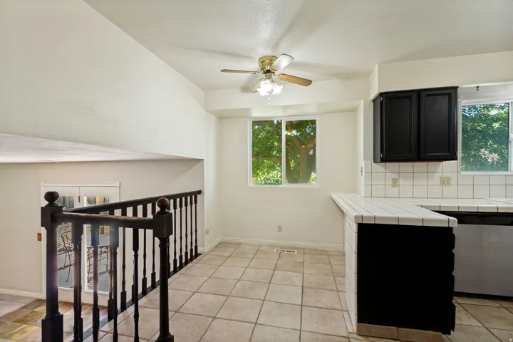 Vaulted ceiling, ceiling fan, white tile flooring, white tile countertops, and black cabinetry