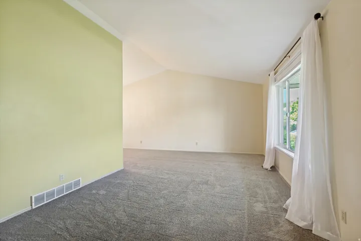 Spacious room with vaulted ceilings, neutral carpeting, and a large window