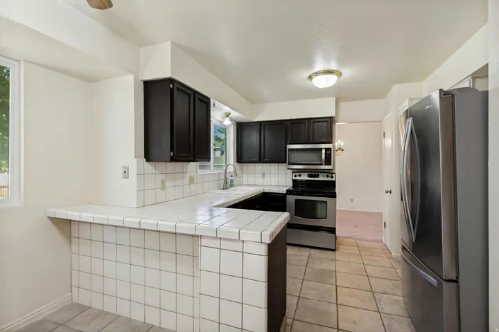 Kitchen featuring white tile countertops, dark cabinetry, stainless steel appliances, and tile flooring