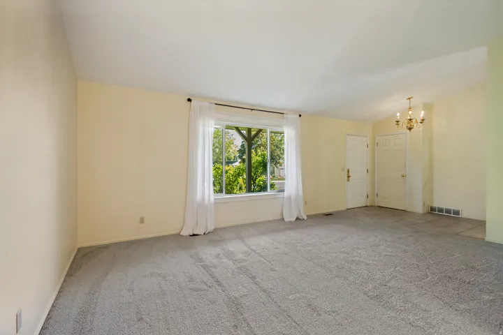 Light gray carpeting, a large picture window, and a decorative chandelier