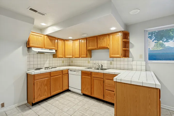 ADU - Kitchen featuring wood cabinetry, white tile countertops and backsplash, an electric stovetop, and a white dishwasher