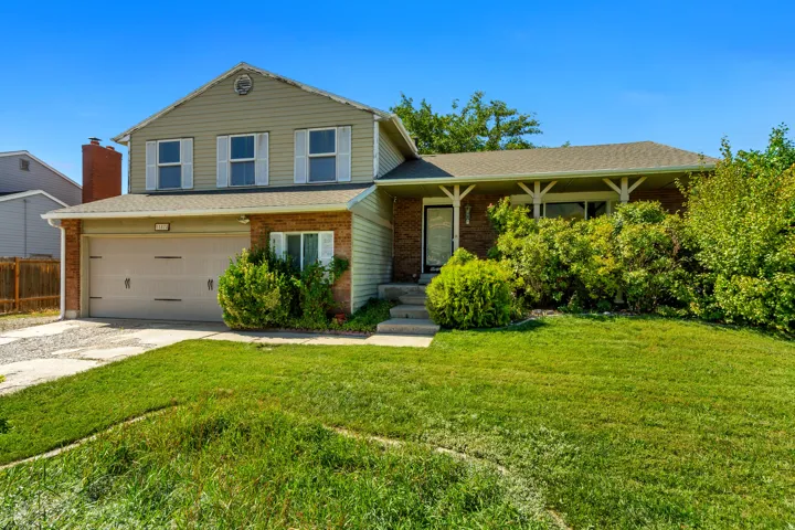 Brick and siding exterior with a two-car garage, mature landscaping, and an inviting front porch