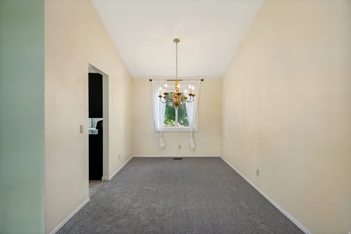 Vaulted ceiling with a brass chandelier, gray carpeting, and window with sheers