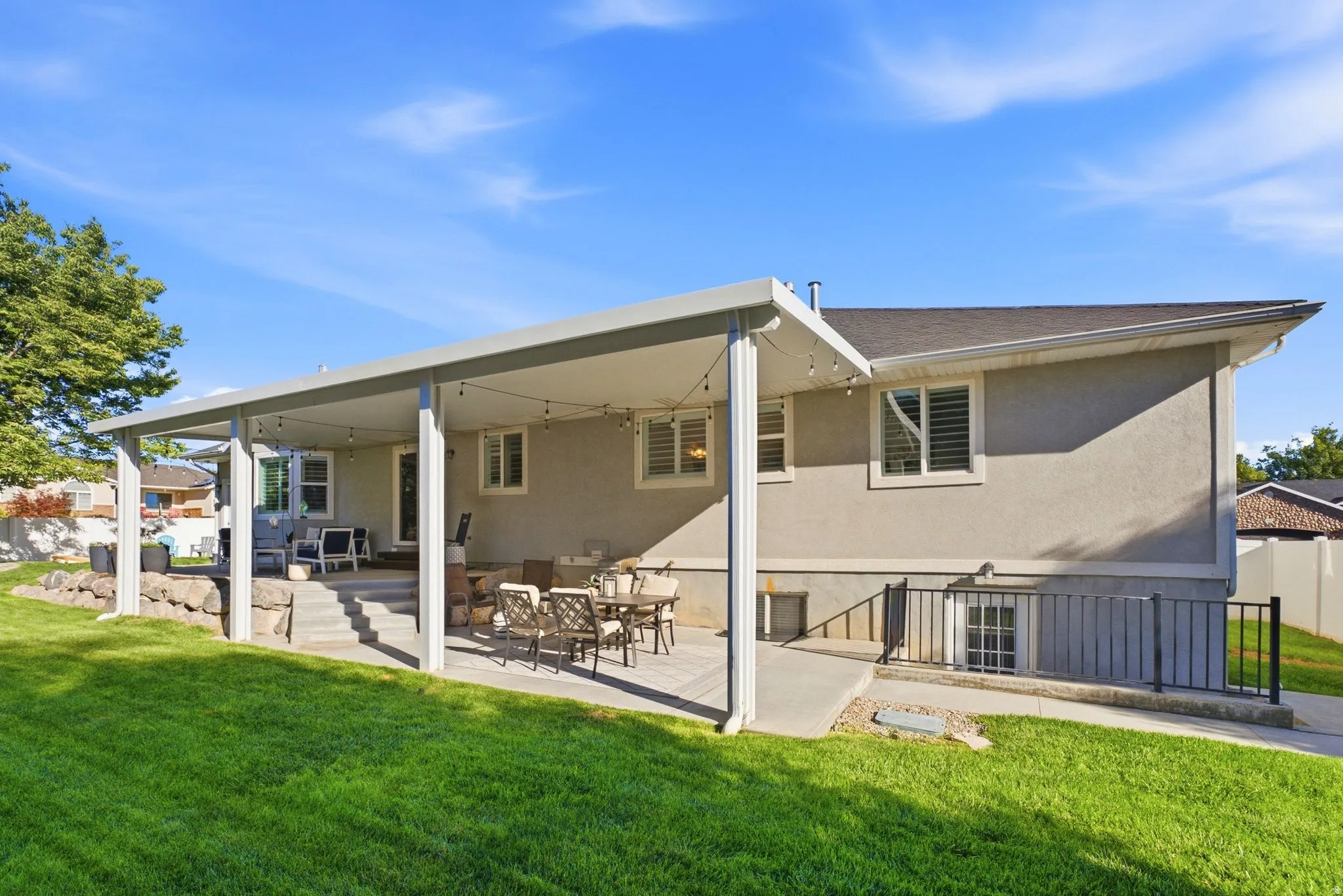 Expansive covered patio with concrete flooring, stucco exterior, and a manicured lawn