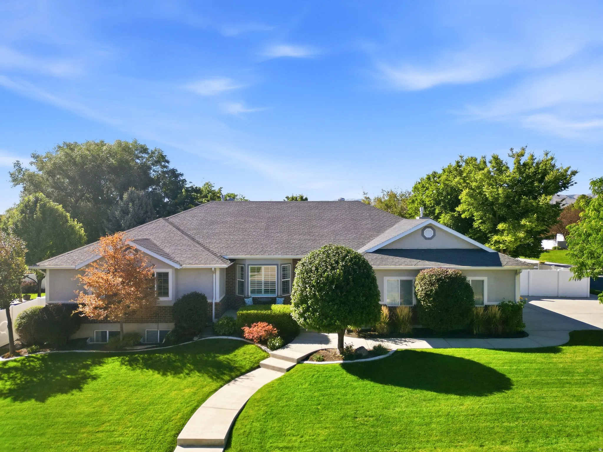 Manicured lawn, mature landscaping, paved driveway, curved walkway, and a multi-level roofline