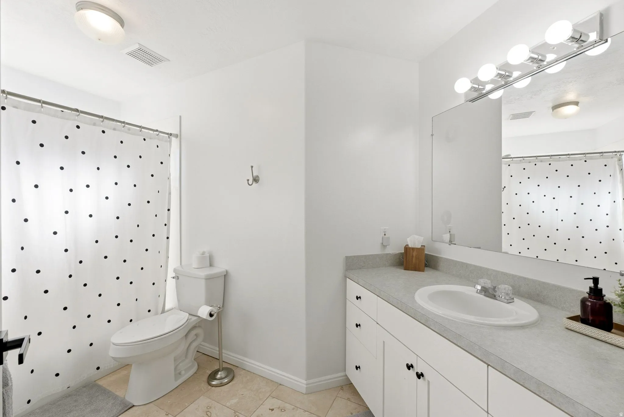 White vanity with a single basin sink and ample counter space, full-width mirror, and a wall-mounted light fixture