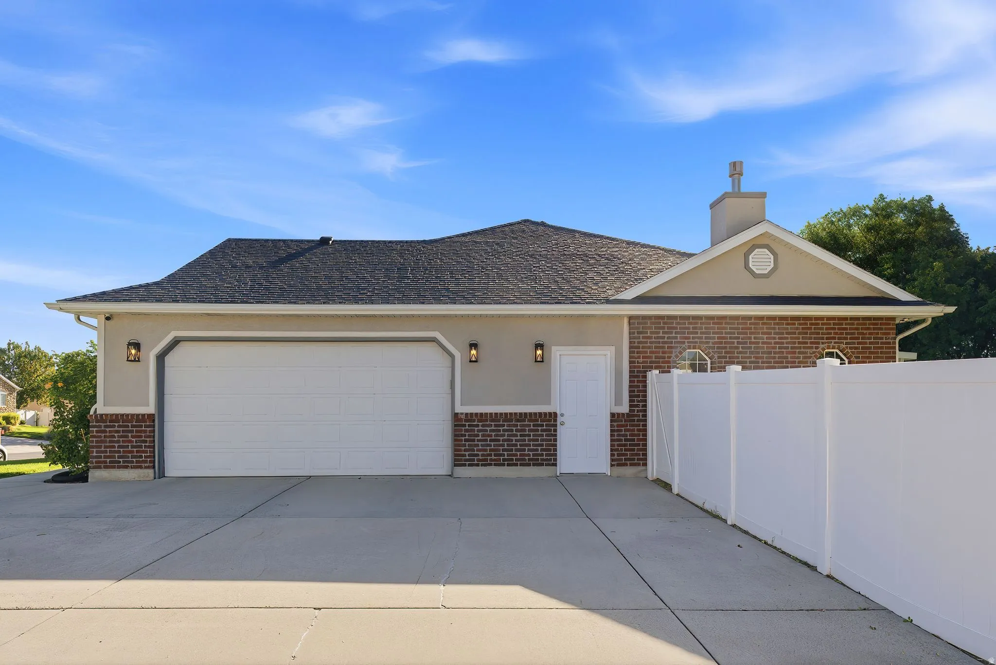 Attached two-car garage with exterior lighting, stucco and brick facade, a separate side entry, and concrete driveway