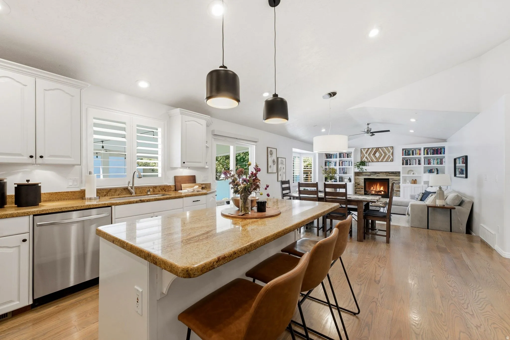 Kitchen island with granite countertop and pendant lighting, white cabinetry, stainless steel dishwasher, wood-finish flooring, and a vaulted ceiling