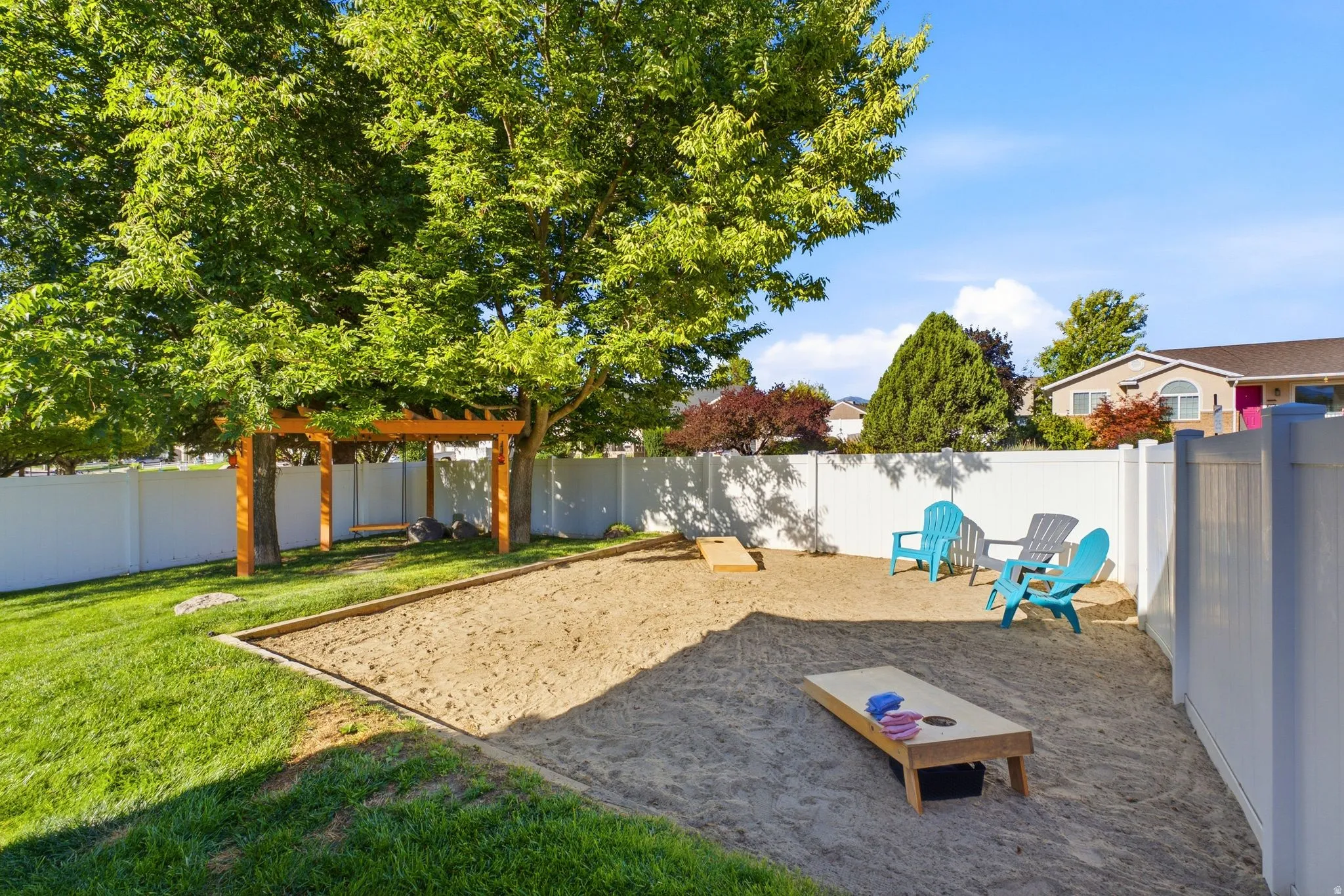 Expansive backyard featuring a manicured lawn, sand area, wood pergola with swing, and white vinyl fencing