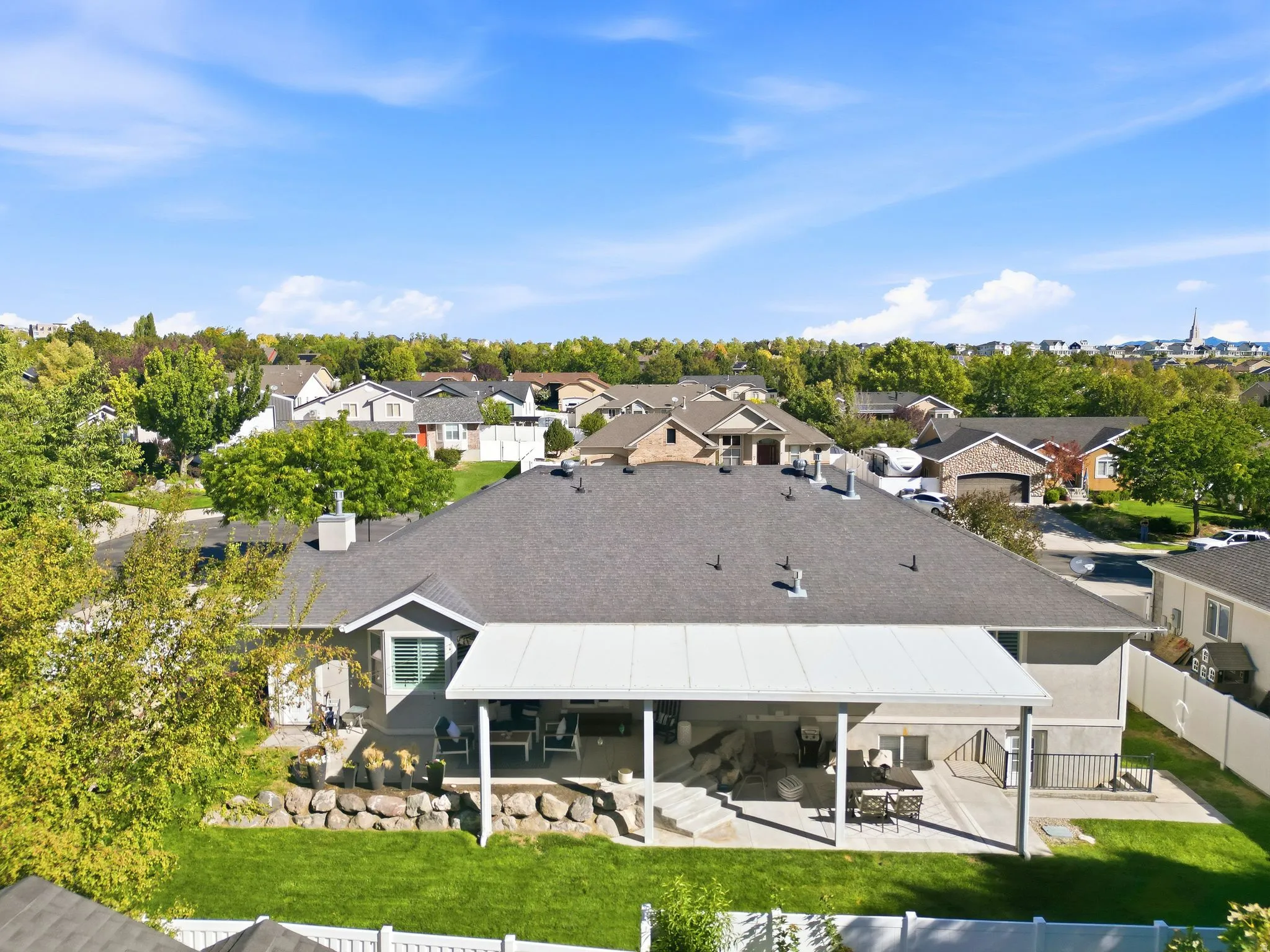 Expansive outdoor patio with a covered section, mature landscaping, and a manicured lawn