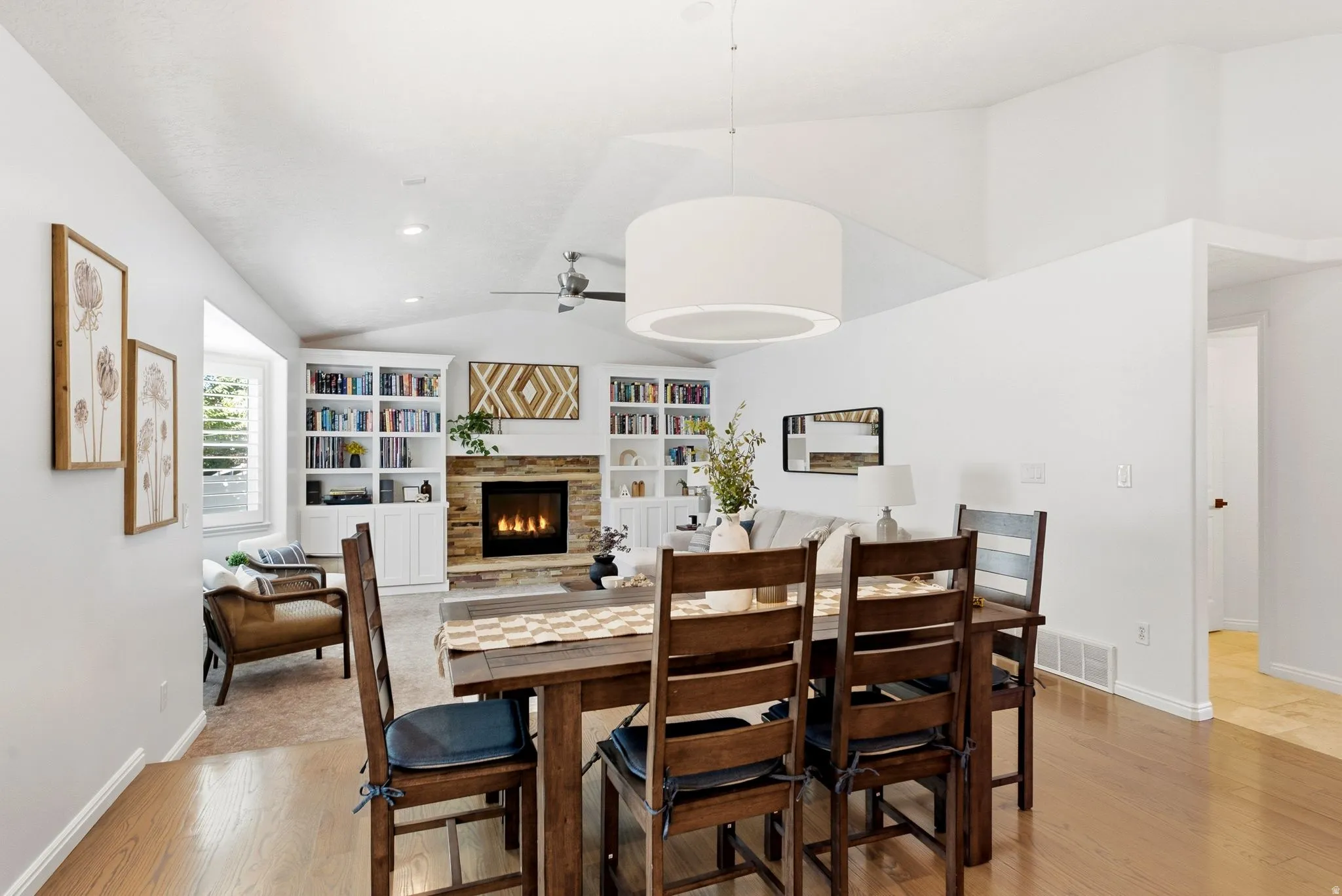 Vaulted ceilings, wood-finish flooring, built-in shelving, stone-clad fireplace, and drum pendant lighting