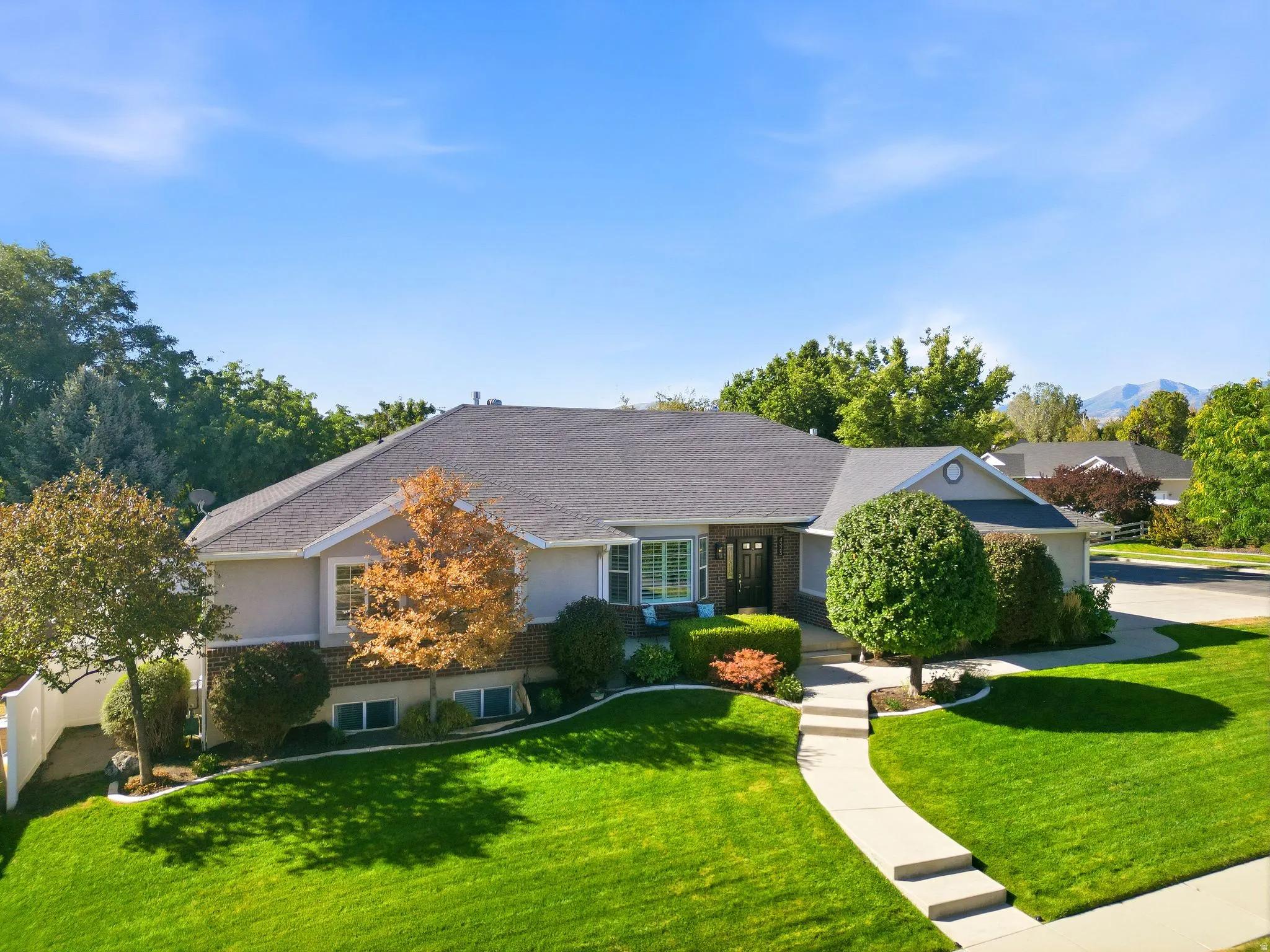 Expansive green lawn, mature trees, concrete walkway, multi-level home, and a dark asphalt roof