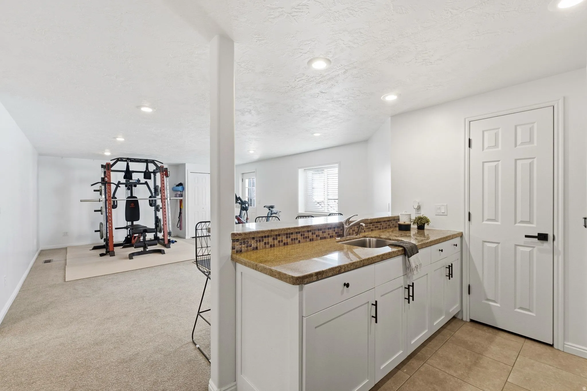 Built-in wet bar with a single-basin sink, mosaic tile backsplash, and white cabinetry