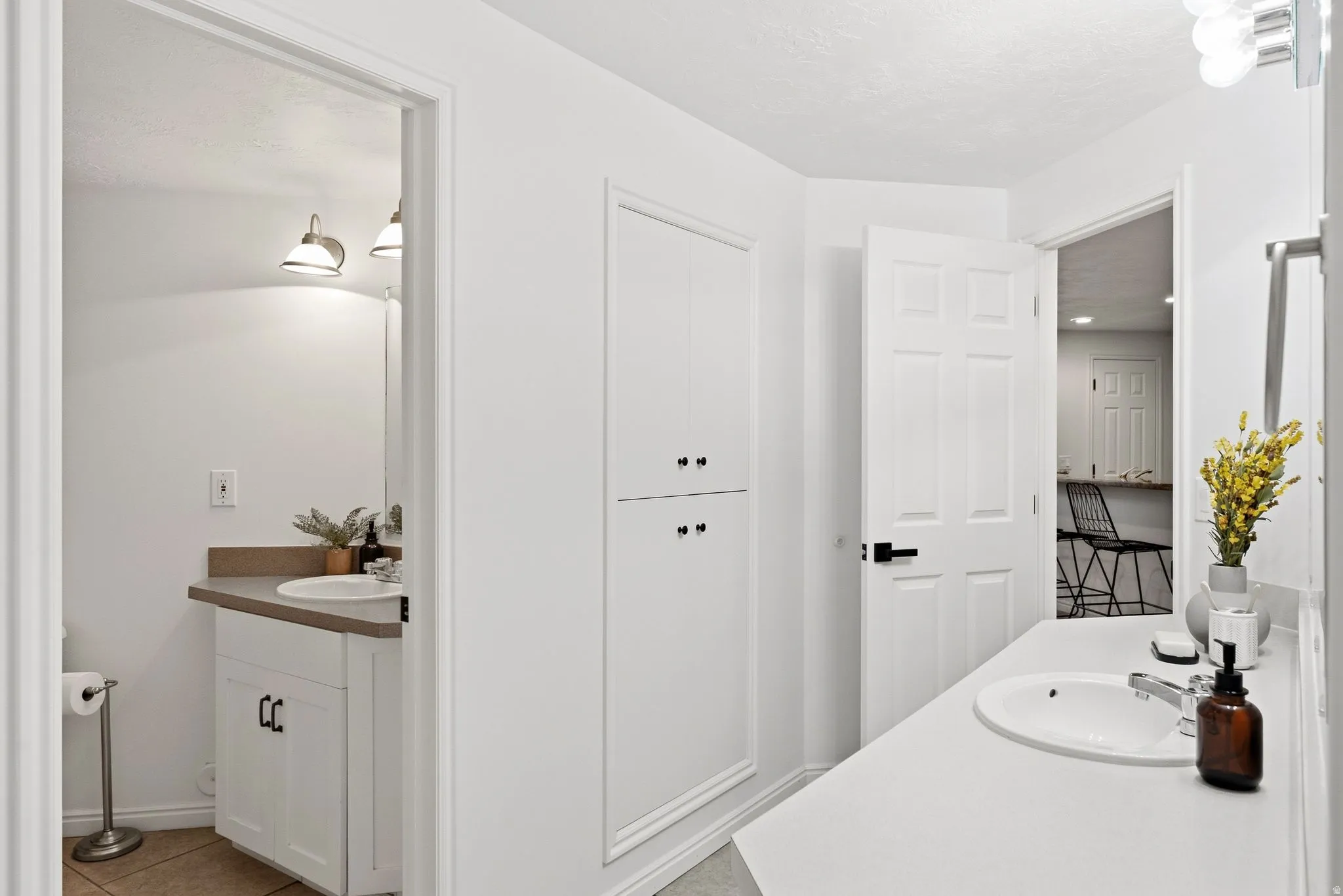 White paneled cabinetry, two vanity sinks with chrome fixtures, built-in storage cabinet, and neutral tile flooring