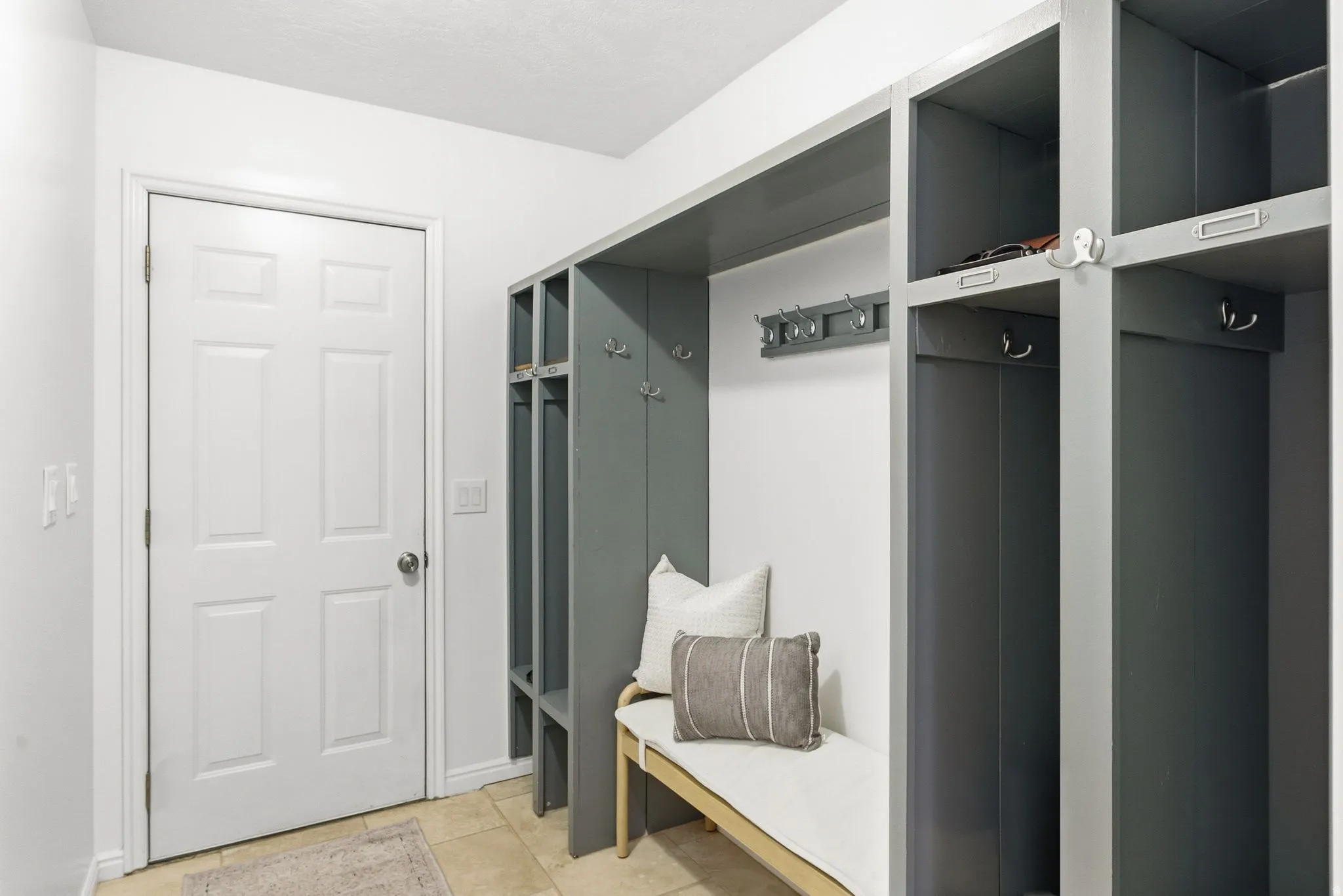 Built-in gray cabinetry with open shelving, integrated hooks, and a built-in bench, complemented by light-toned tile flooring