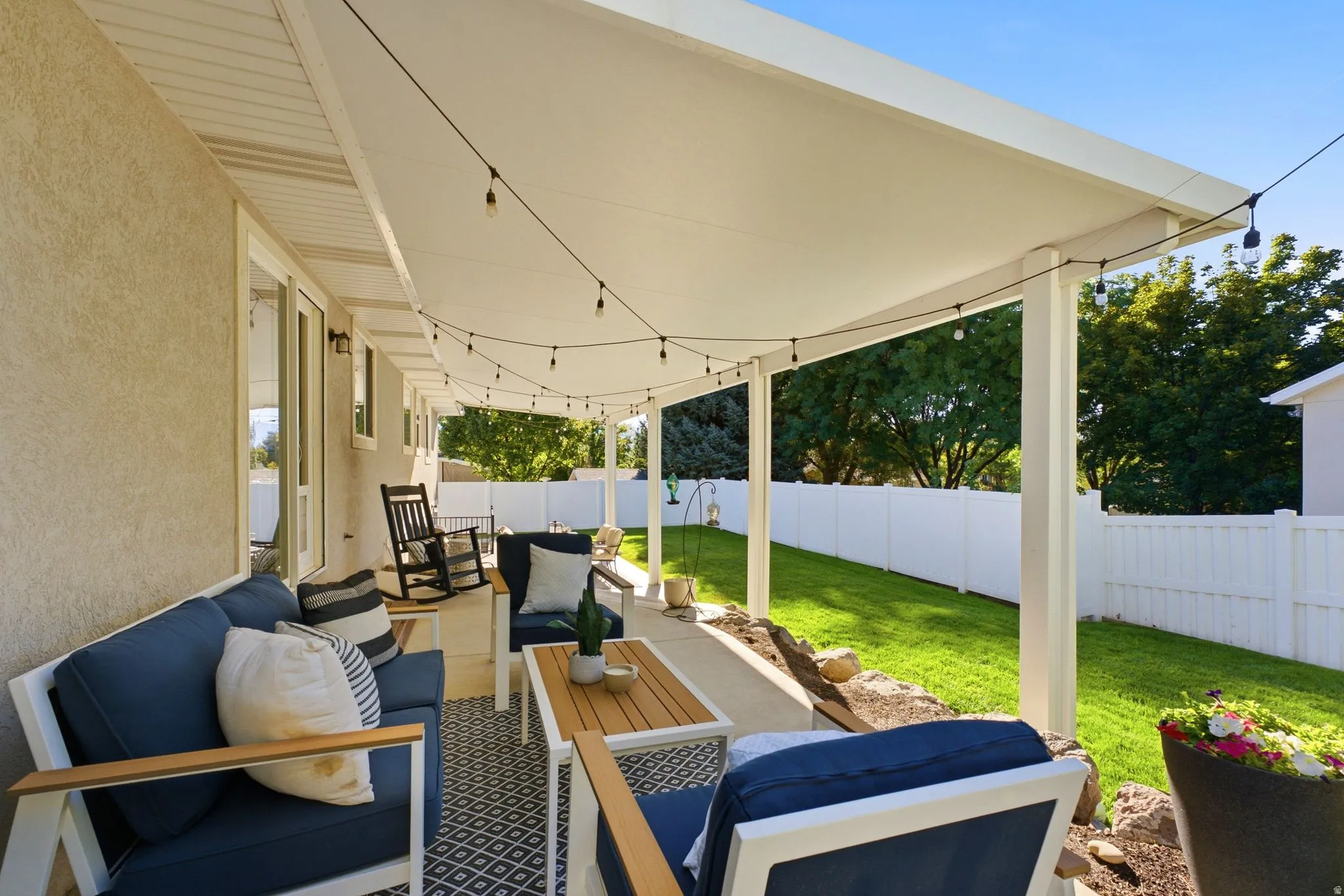 Covered patio with string lighting, stucco exterior, and bright green lawn