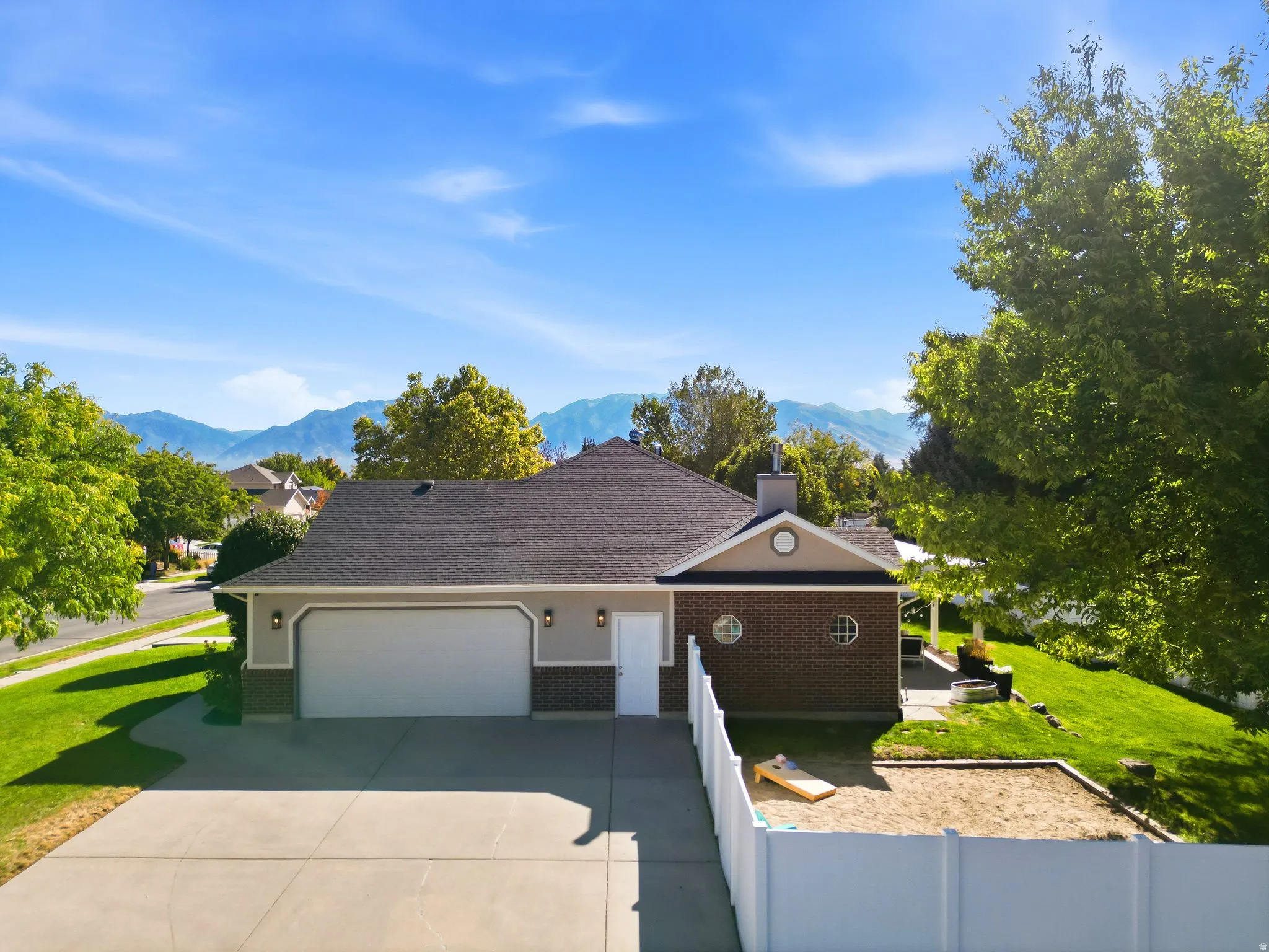 Exterior showcasing a dual-car garage, brick and siding facade, circular windows, a paved driveway, and a fenced yard