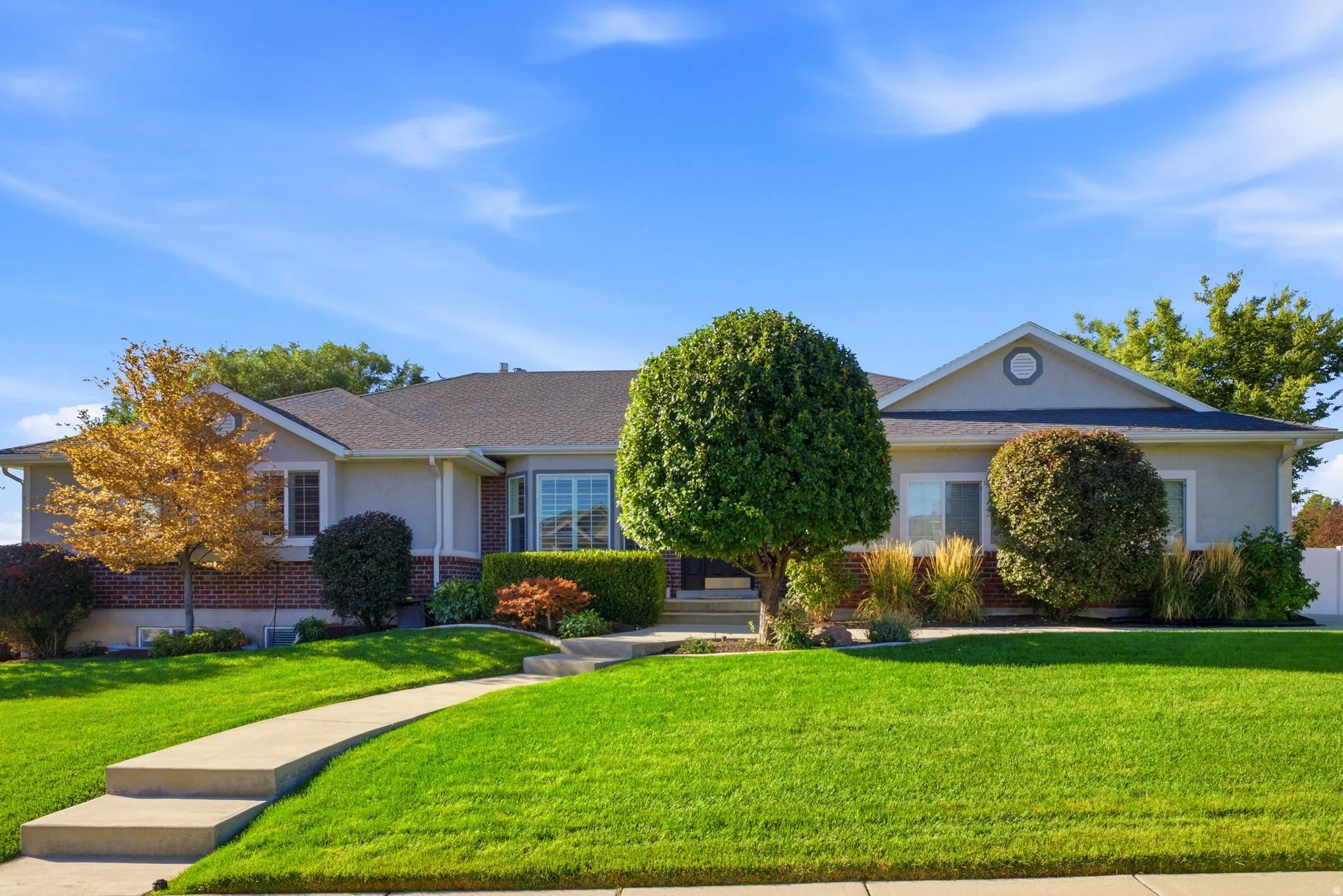 Stucco and brick exterior with a gabled roof, prominent bay window, and concrete walkway