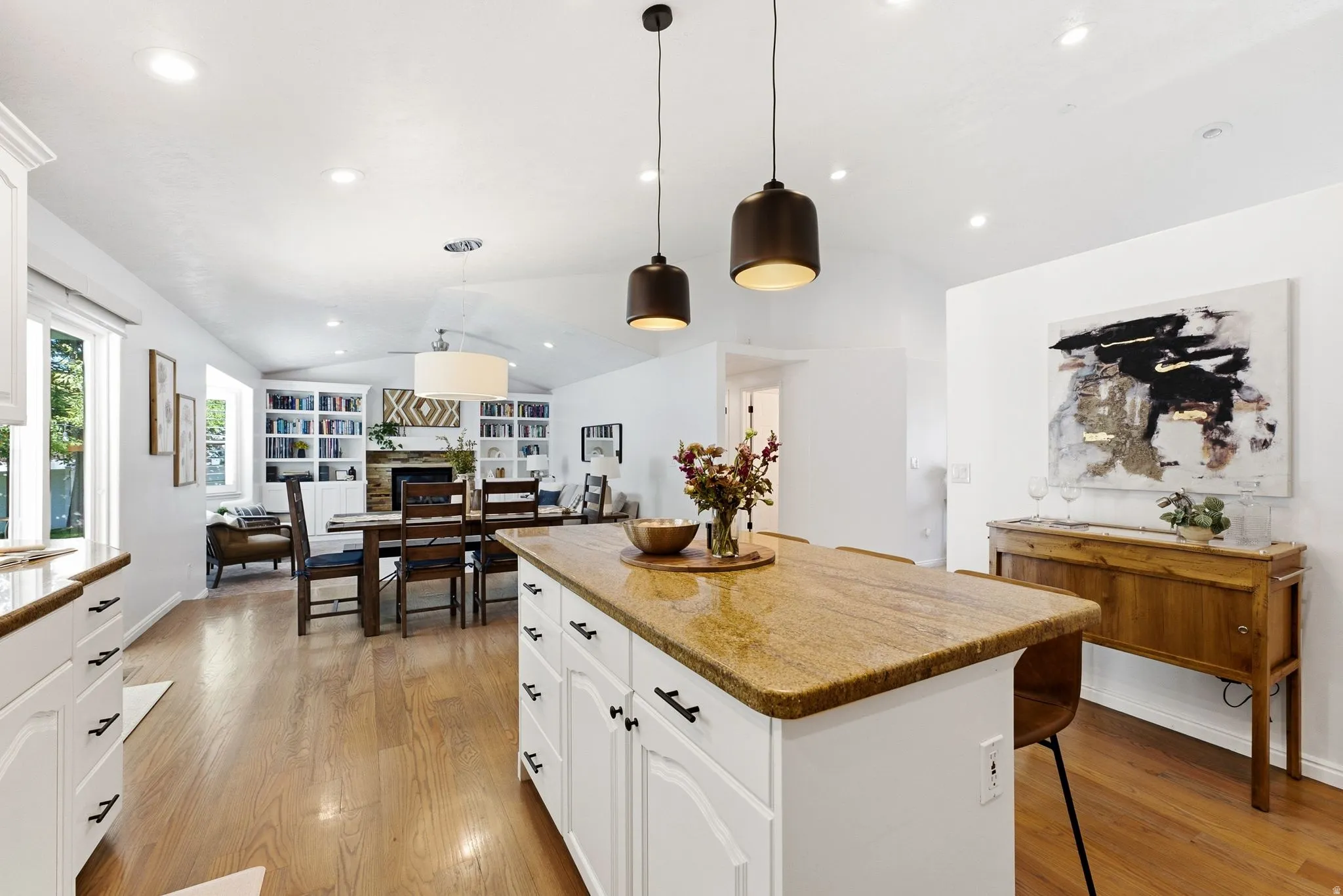 Open-concept living area featuring wood-finish flooring, white cabinetry, a kitchen island with a stone countertop, and recessed lighting