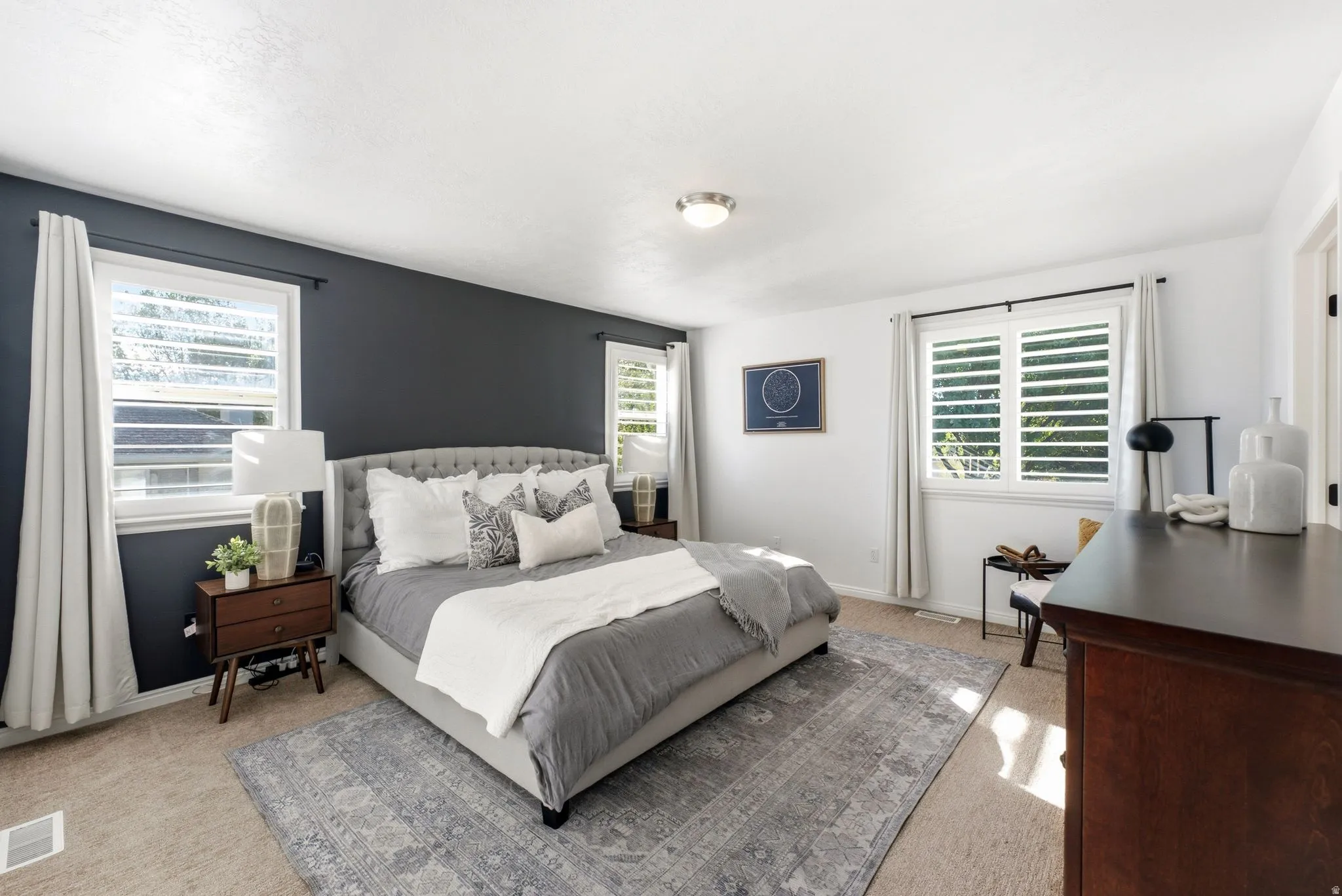 Spacious room featuring white walls and a contrasting accent wall, two windows with white plantation shutters, and a flush mount ceiling light