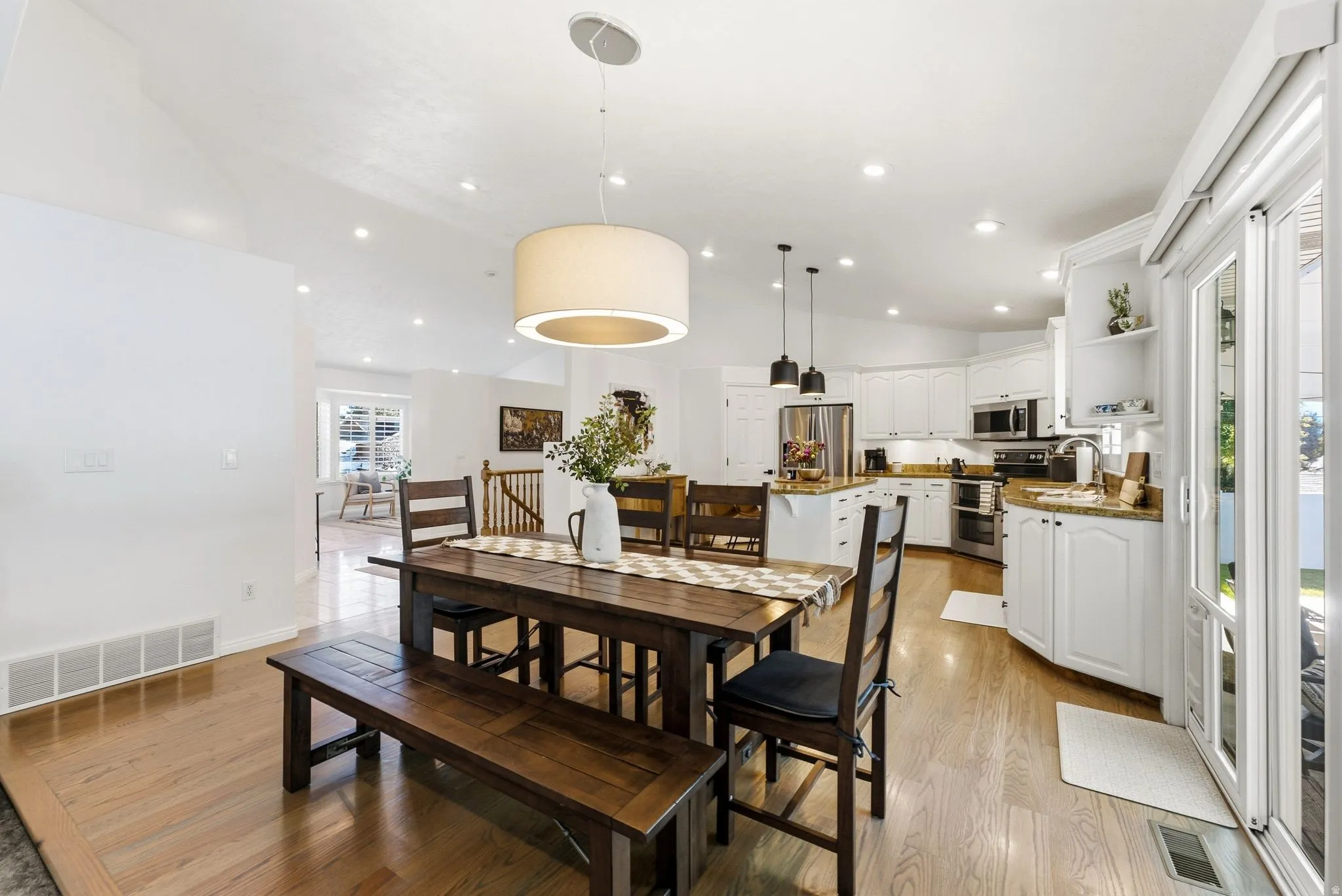 Light wood-finish flooring, vaulted ceiling, recessed lighting, white cabinetry, and stainless steel appliances
