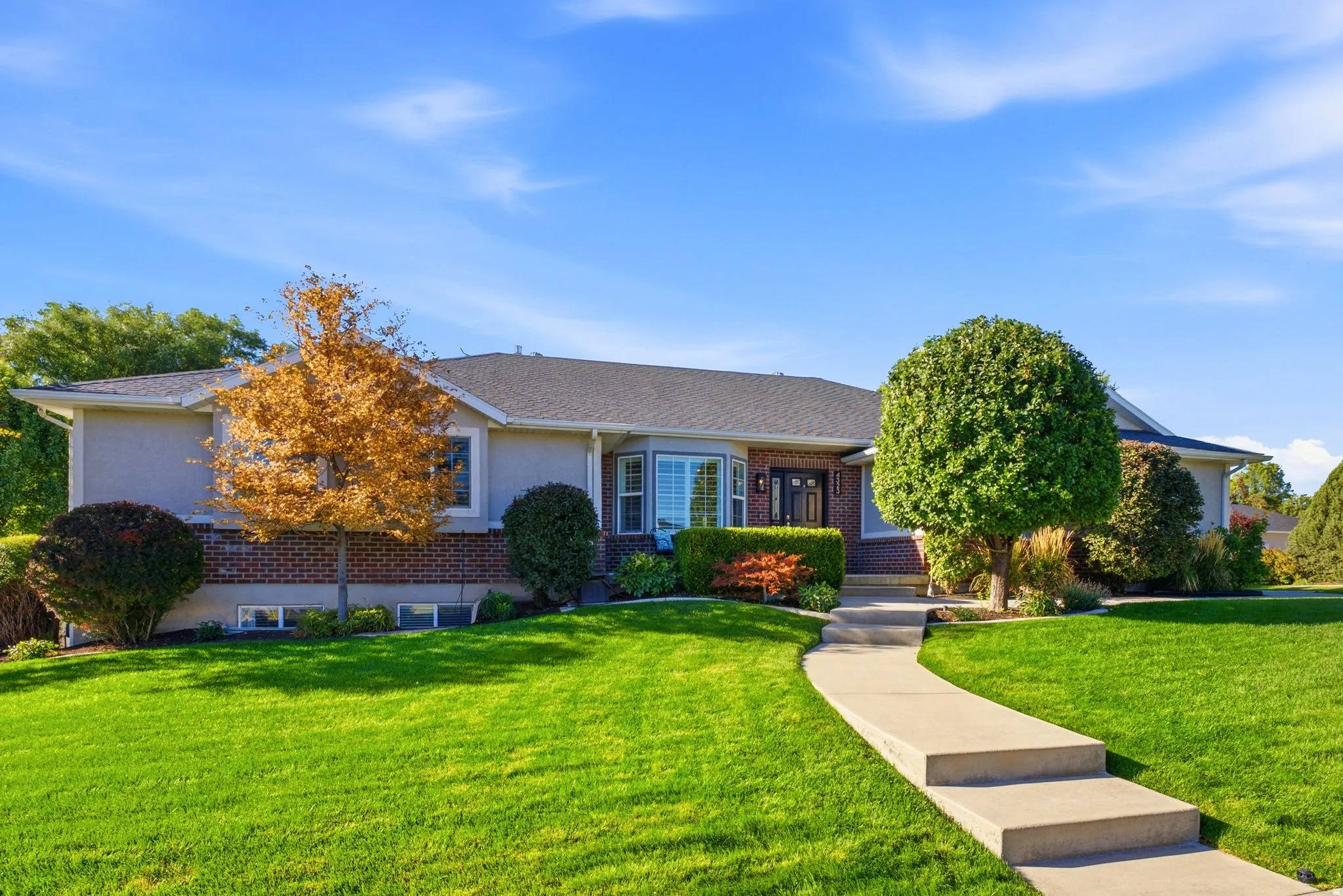 Exterior featuring a bay window, brick and stucco siding, a dark roof, and a concrete pathway