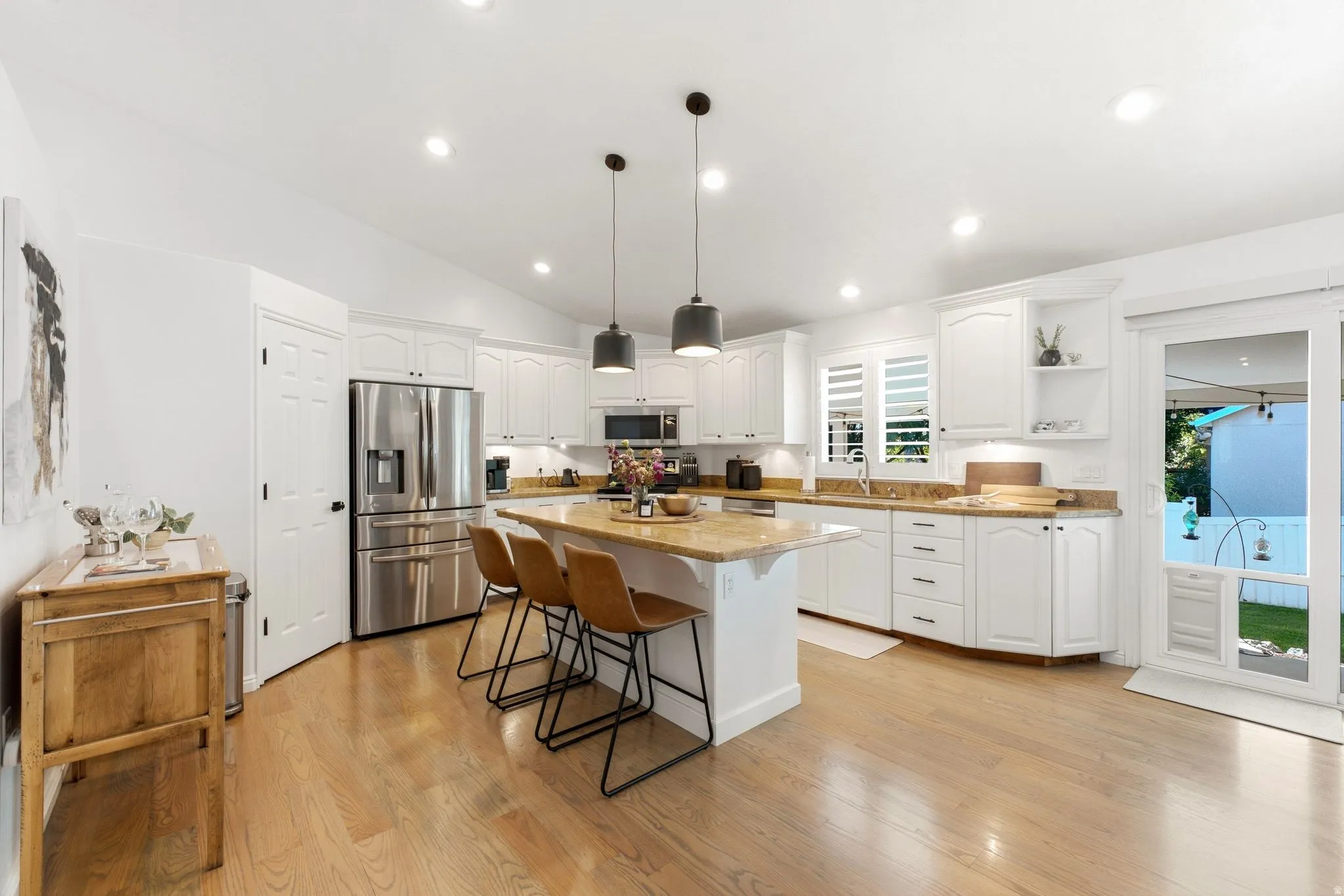 Recessed lighting, wood-finish flooring, white cabinetry, integrated stainless steel appliances, and a central island with pendant lighting
