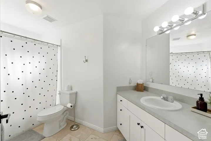 White vanity with a single basin sink and ample counter space, full-width mirror, and a wall-mounted light fixture
