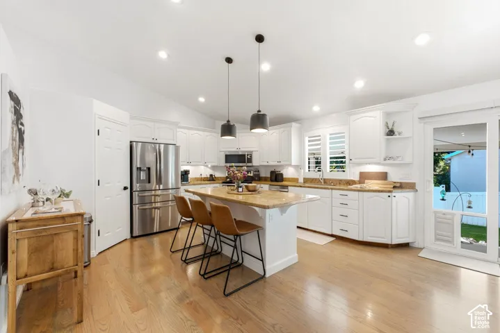 Recessed lighting, wood-finish flooring, white cabinetry, integrated stainless steel appliances, and a central island with pendant lighting