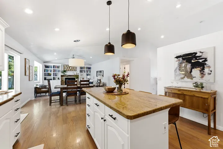 Open-concept living area featuring wood-finish flooring, white cabinetry, a kitchen island with a stone countertop, and recessed lighting