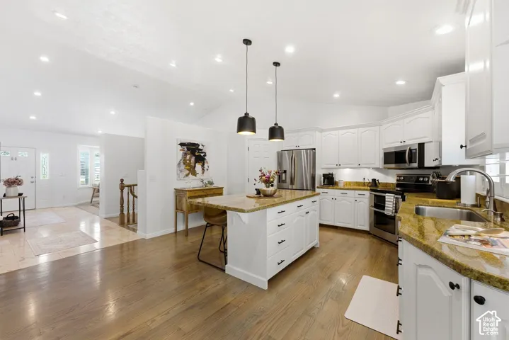 Kitchen featuring wood-finish flooring, white cabinetry, a center island with countertop, and stainless steel appliances
