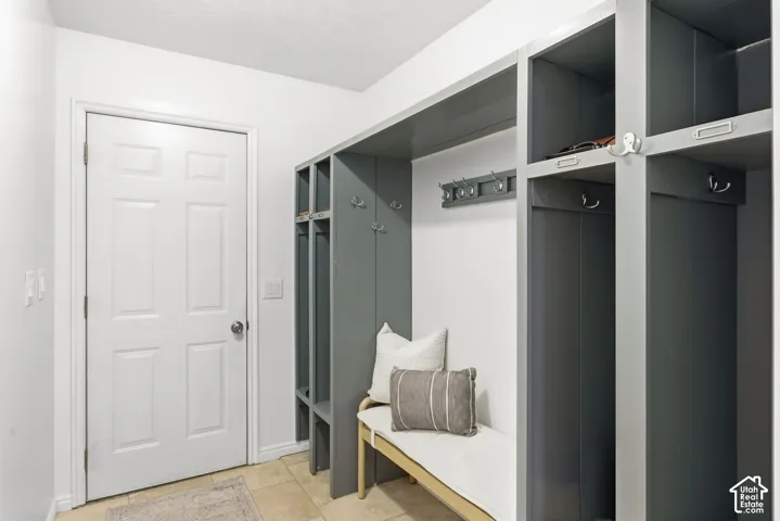 Built-in gray cabinetry with open shelving, integrated hooks, and a built-in bench, complemented by light-toned tile flooring