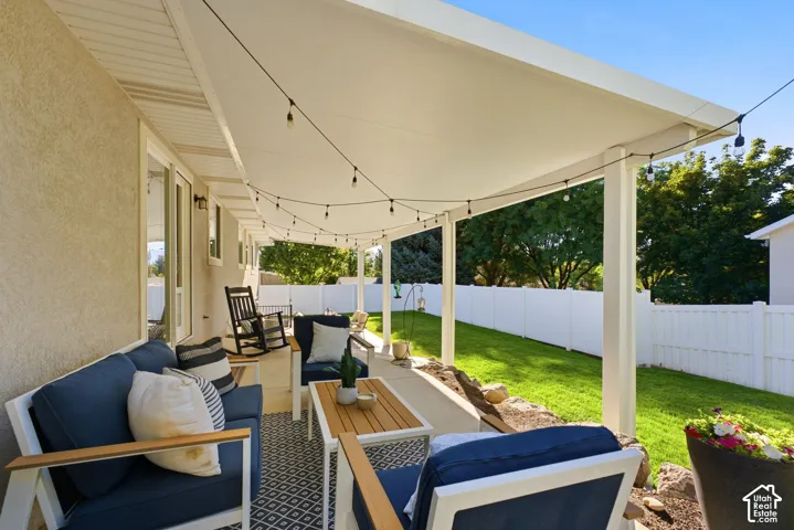 Covered patio with string lighting, stucco exterior, and bright green lawn