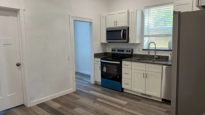 Modern kitchen featuring white shaker-style cabinetry, granite-patterned countertops, stainless steel appliances, and wood-finish flooring