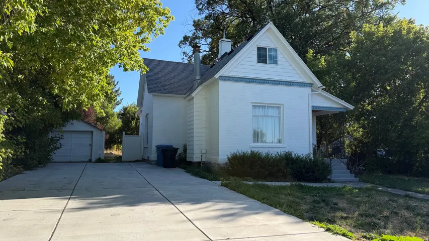 Traditional white brick exterior with a gray shingle roof, featuring a covered front porch, a gabled dormer, and a detached single-car garage